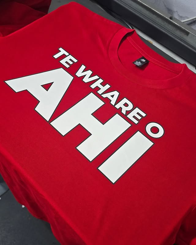 Bold red Te Whare o Ahi t-shirt with large white printed type across the front